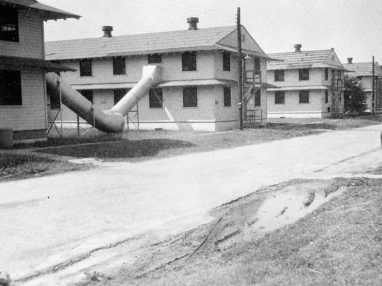 black and white photograph of row of two-story buildings with tube-like evacuation slides on the upper floors